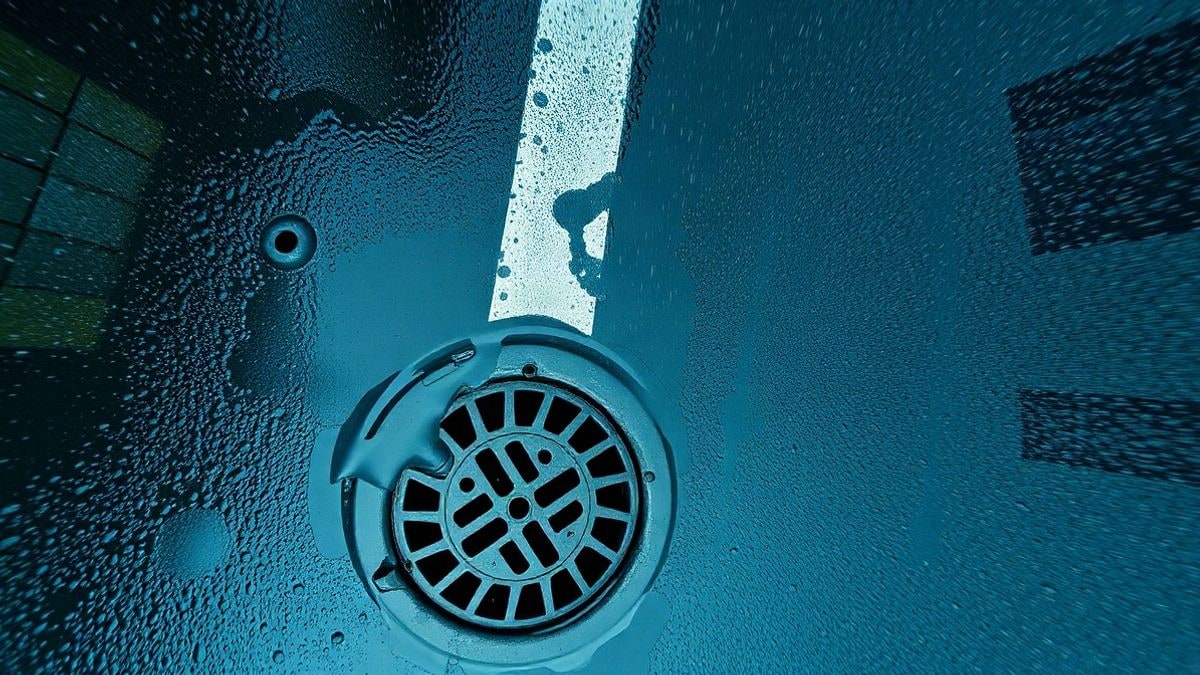Imagen ilustrativa: vista cenital de la lluvia cayendo sobre un desagüe de una calle mojada con charcos