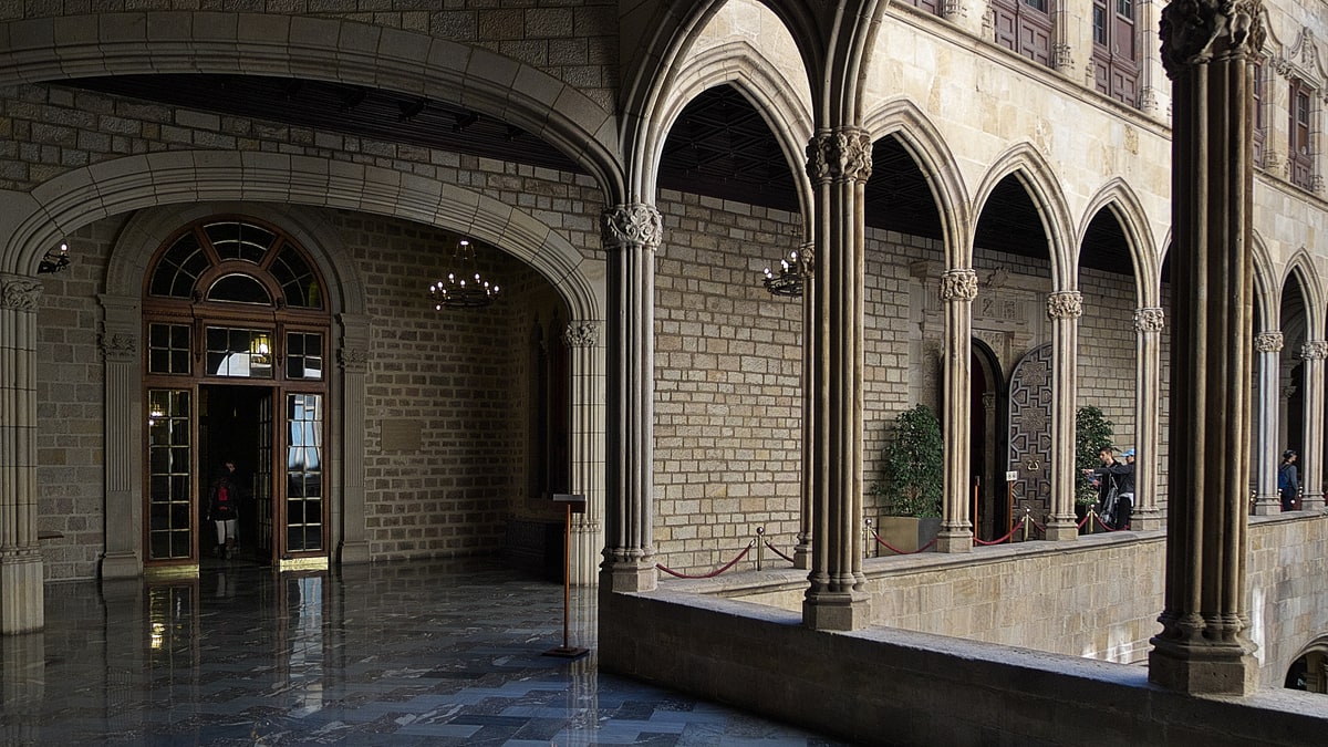Galería gótica del Ayuntamiento de Barcelona con arcos de piedra, columnas y suelo de mármol pulido.