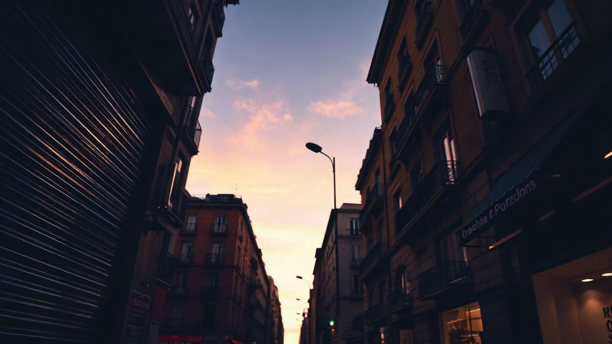 Illustrative image: empty city street at sunset, with closed shop shutters and lit street lamps
