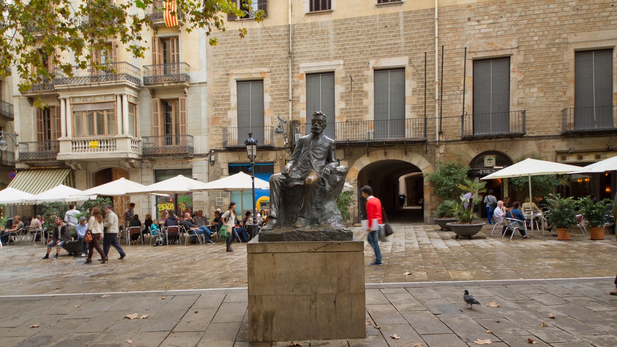 Bronze statue of a seated writer in a Gothic square with terraces in the background
