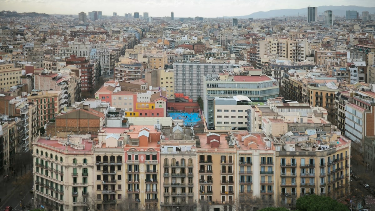 Aerial view of residential buildings and rooftops in Barcelona with trees in the foreground.