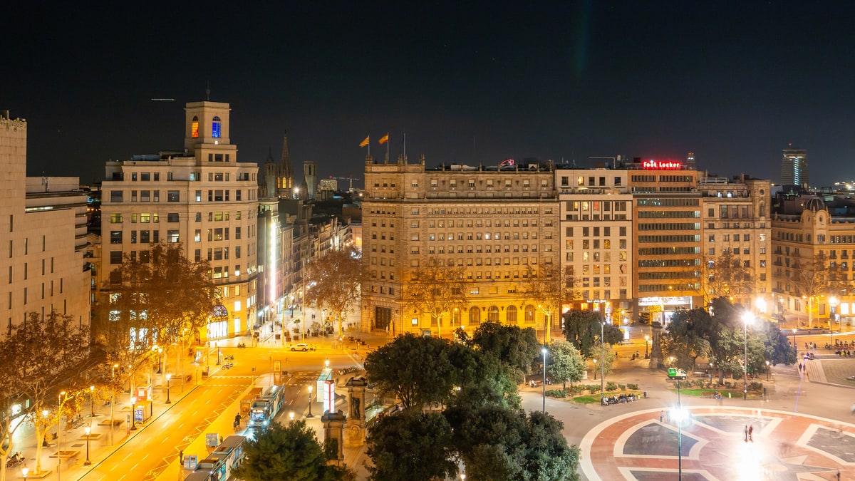 Vista nocturna de la plaza de Catalunya de Barcelona con tráfico y edificios iluminados
