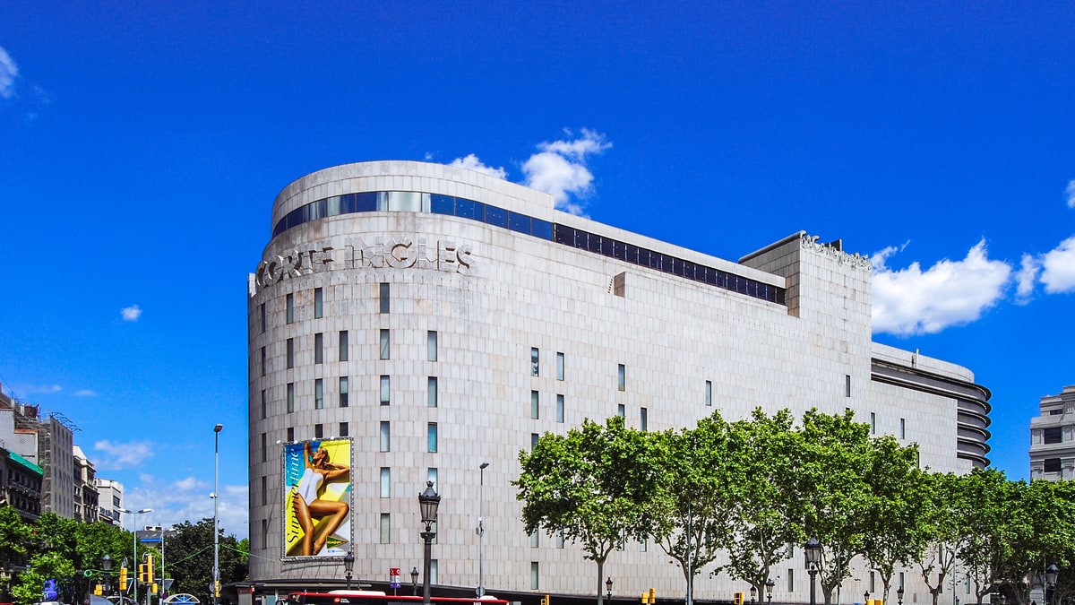 El Corte Inglés de la plaza de Catalunya bajo cielo azul despejado, con motos aparcadas y peatones
