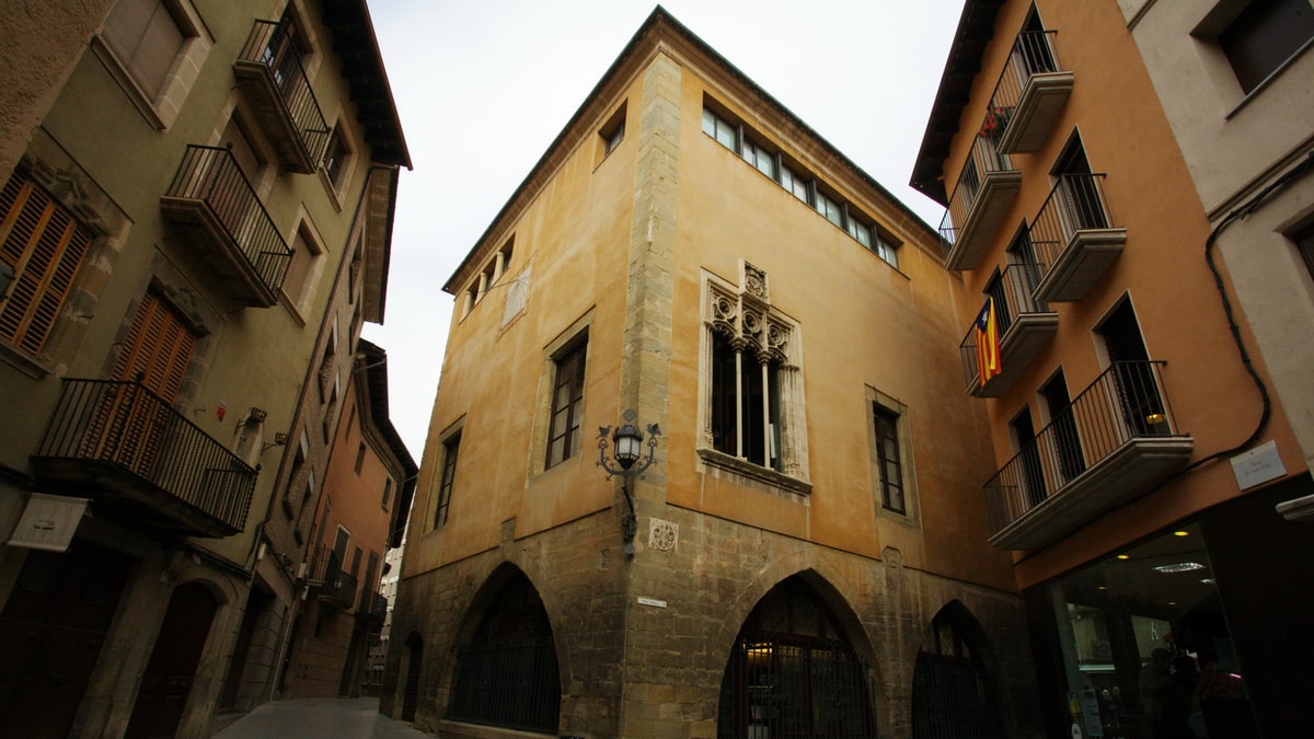 Gothic facade of the Llotja de Vic with pointed arches and an ornate corner window.