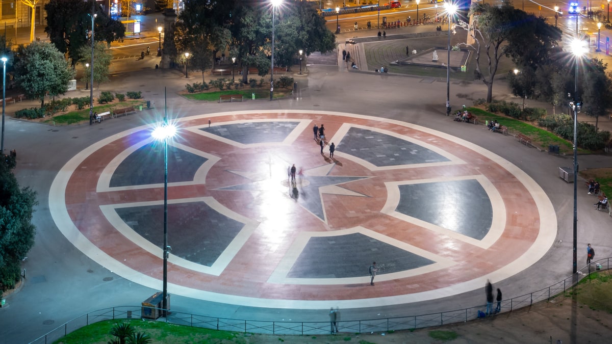 Plaza de Catalunya de noche, con su gran rosa de los vientos y paseantes iluminados por farolas