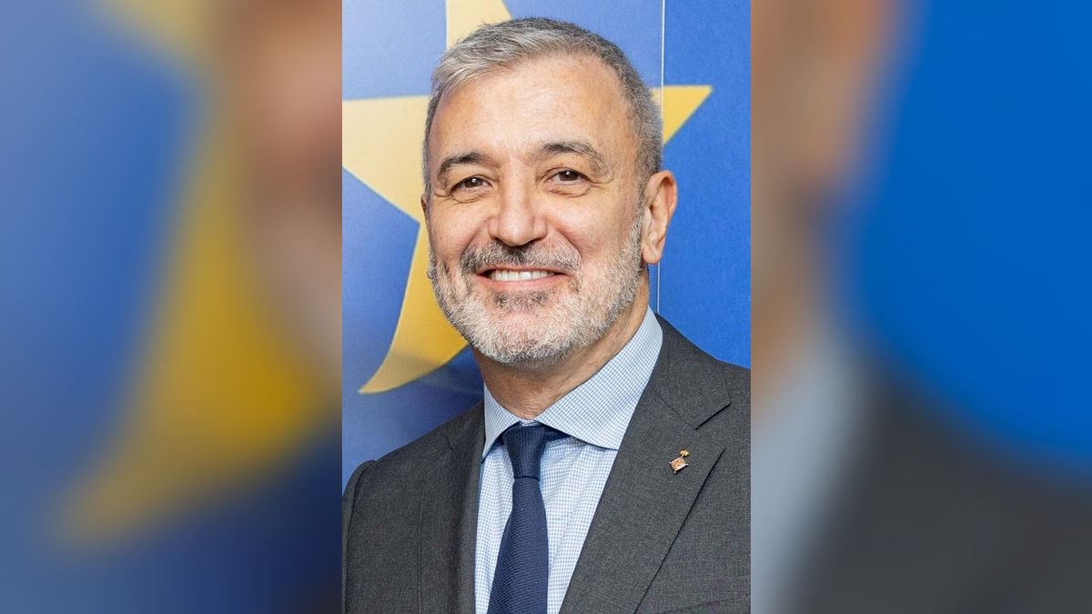 Retrato sonriente de Jaume Collboni con traje oscuro y corbata azul ante fondo azul con estrella dorada