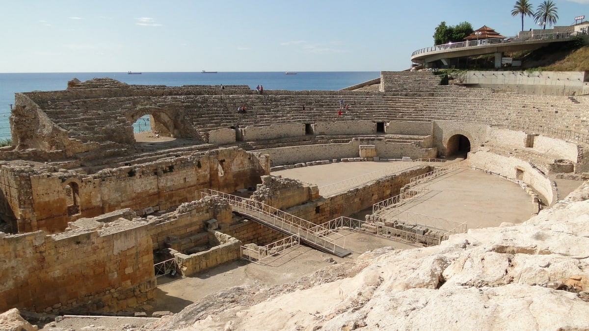 Anfiteatro romano de Tarragona con gradas de piedra y el mar Mediterráneo al fondo.