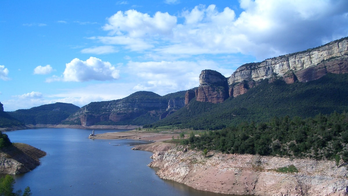 Embalse de Sau con orillas rocosas expuestas y cielo azul con nubes
