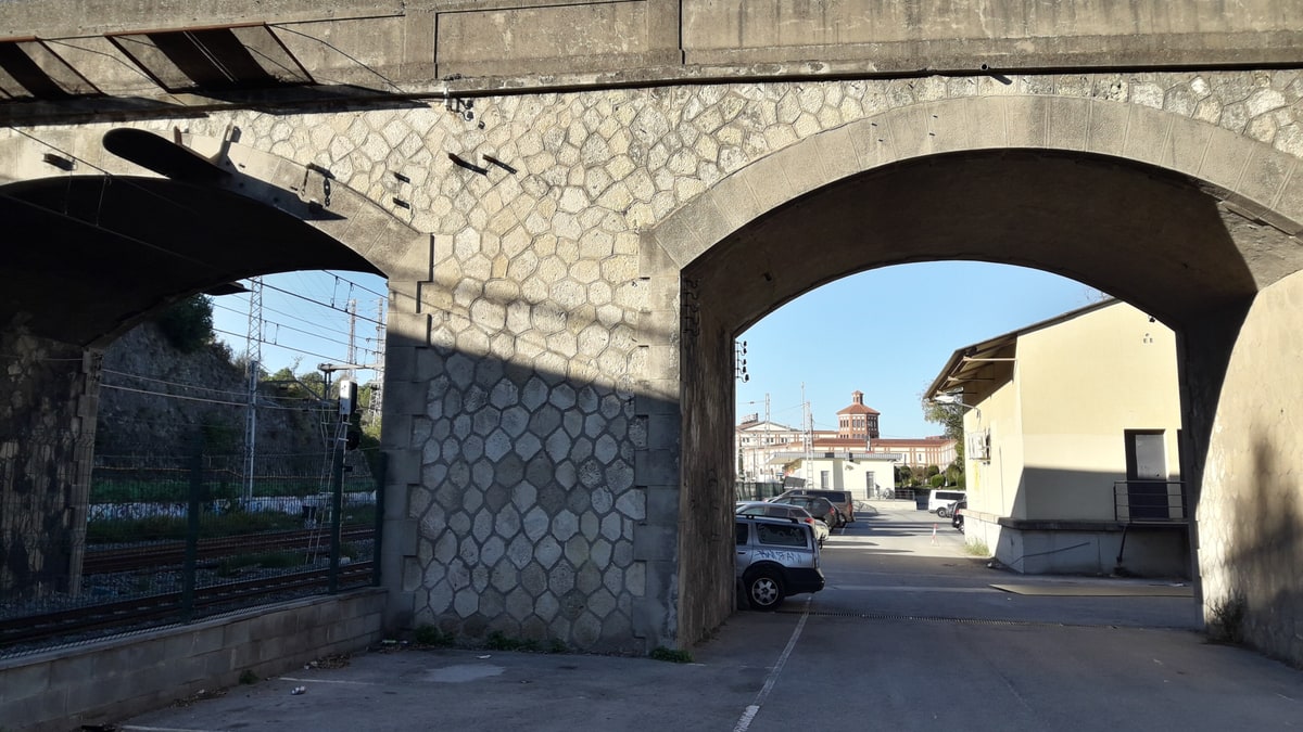 Stone bridge arch over street in Sant Sadurní d'Anoia with parked car.