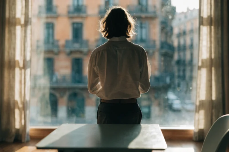 Persona de espaldas mirando por una ventana grande hacia un edificio de apartamentos en Barcelona.